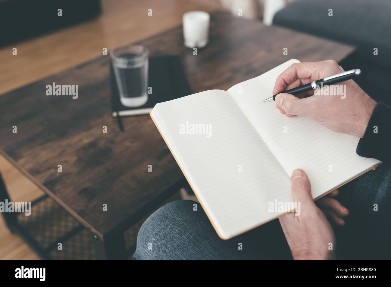 high angle view of man sitting on sofa taking notes in diary or journal on his legs Stock Photo