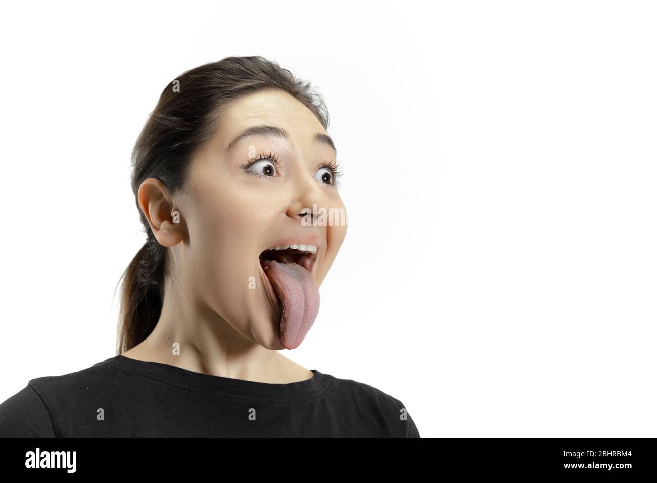 Smiling girl opening her mouth and showing the long big giant tongue isolated on white background. Looks shocked, attracted, wondered and astonished. Copyspace for ad. Human emotions, marketing. Stock Photo