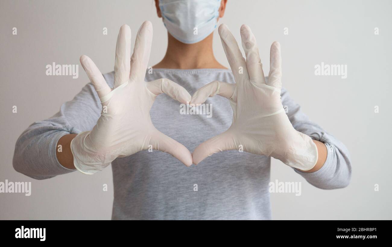 A nurse with a medical mask and gloves gives a symbol of the heart ...