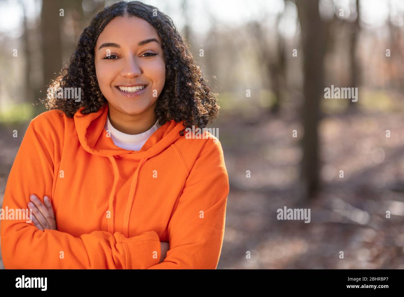 Outdoor portrait of beautiful happy mixed race biracial African American girl teenager female young woman arms folded laughing and smiling with perfec Stock Photo