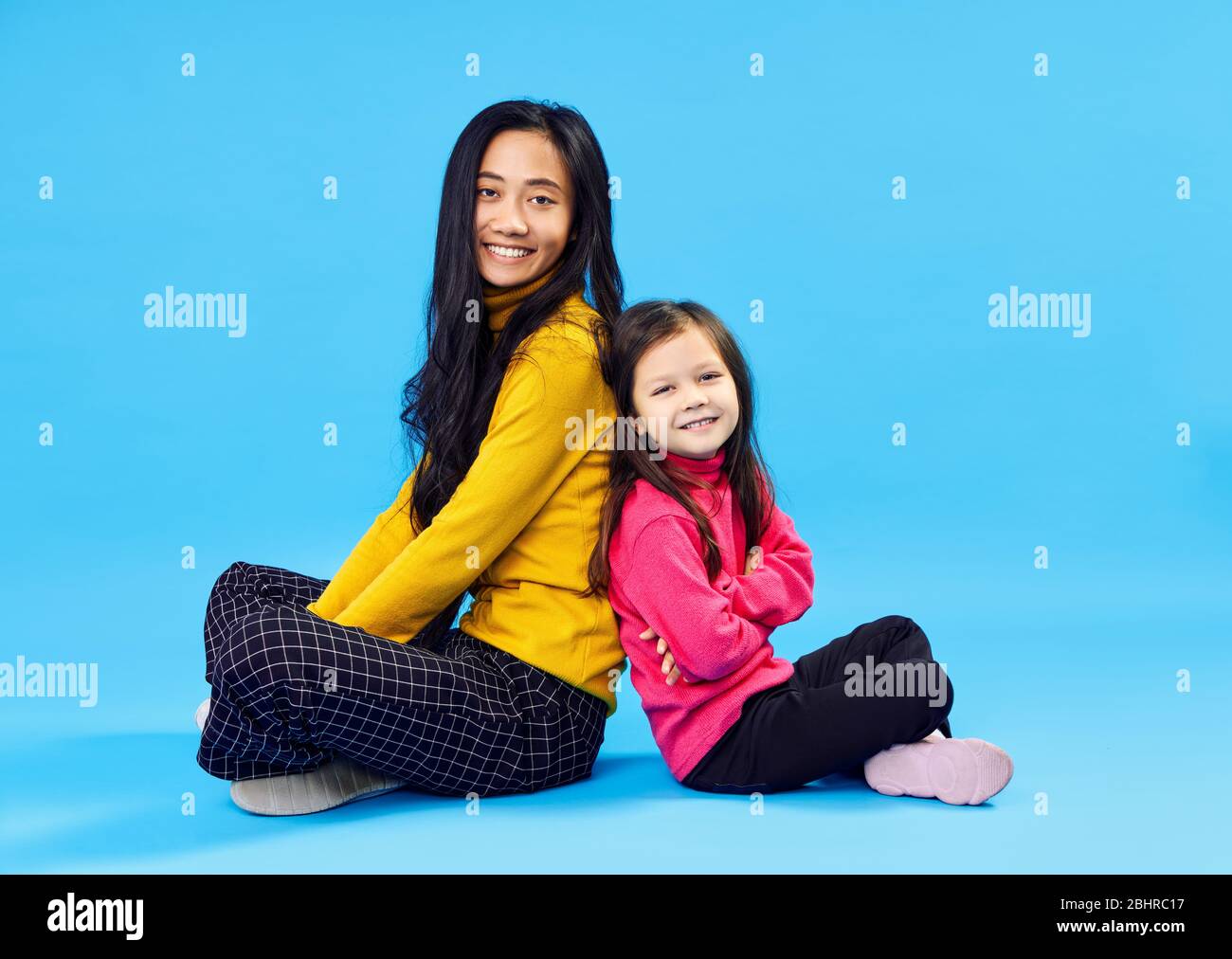 Happy smiling mother and her little cute daughter posing on blue studio background Stock Photo