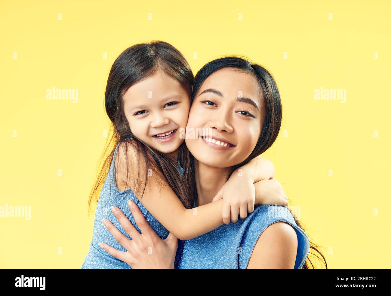 Happy mother and her child daughter hugging on yellow background. Family, embrace concept Stock Photo