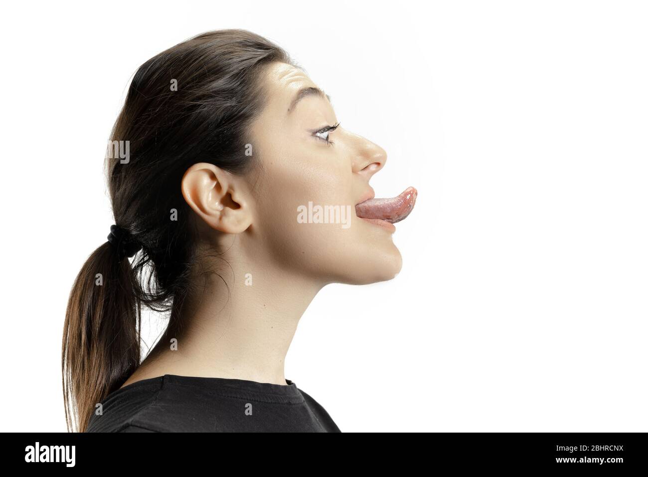 Smiling girl opening her mouth and showing the long big giant tongue isolated on white background. Looks shocked, attracted, wondered and astonished. Copyspace for ad. Human emotions, marketing. Stock Photo