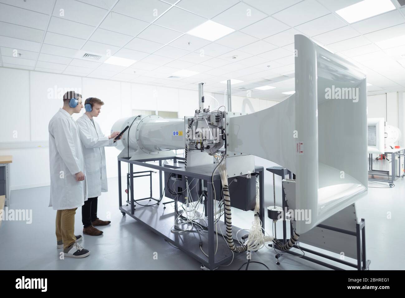 Two male scientists wearing white lab coats performing experiment in wind tunnel in research