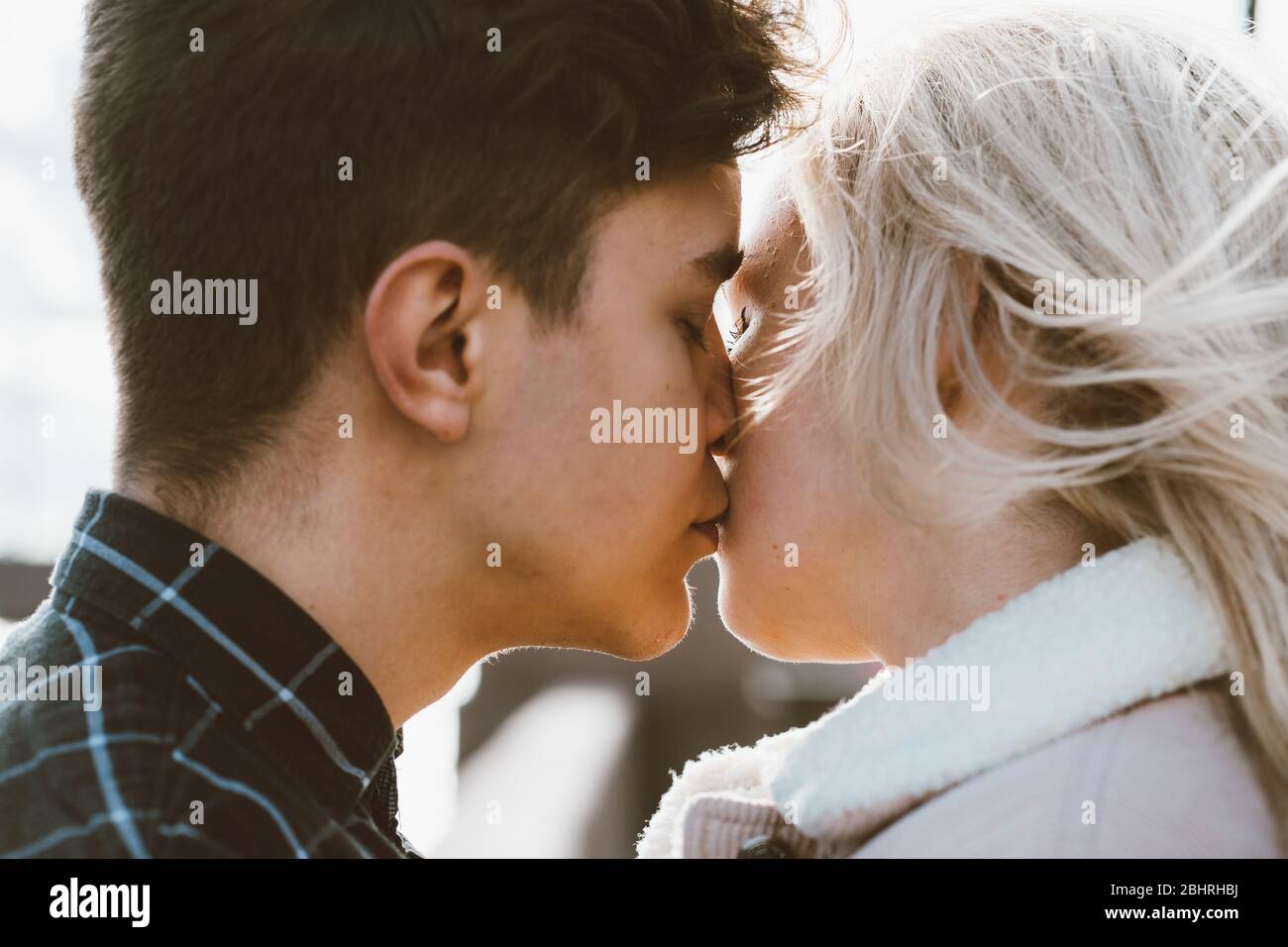 The boy looks tenderly at girl and wants to kiss. A young couple stands embracing. The concept of teenage love and first kiss, sincere feelings of man Stock Photo