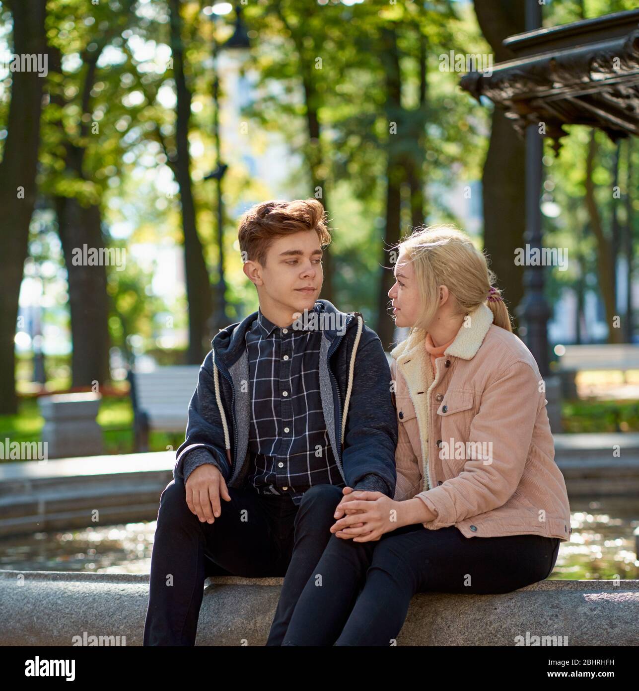 Lovers boy and girl look at each other, sitting in the Park near the fountain in the fall. Girlfriend and Boyfriend are talking concept of love and Stock Photo