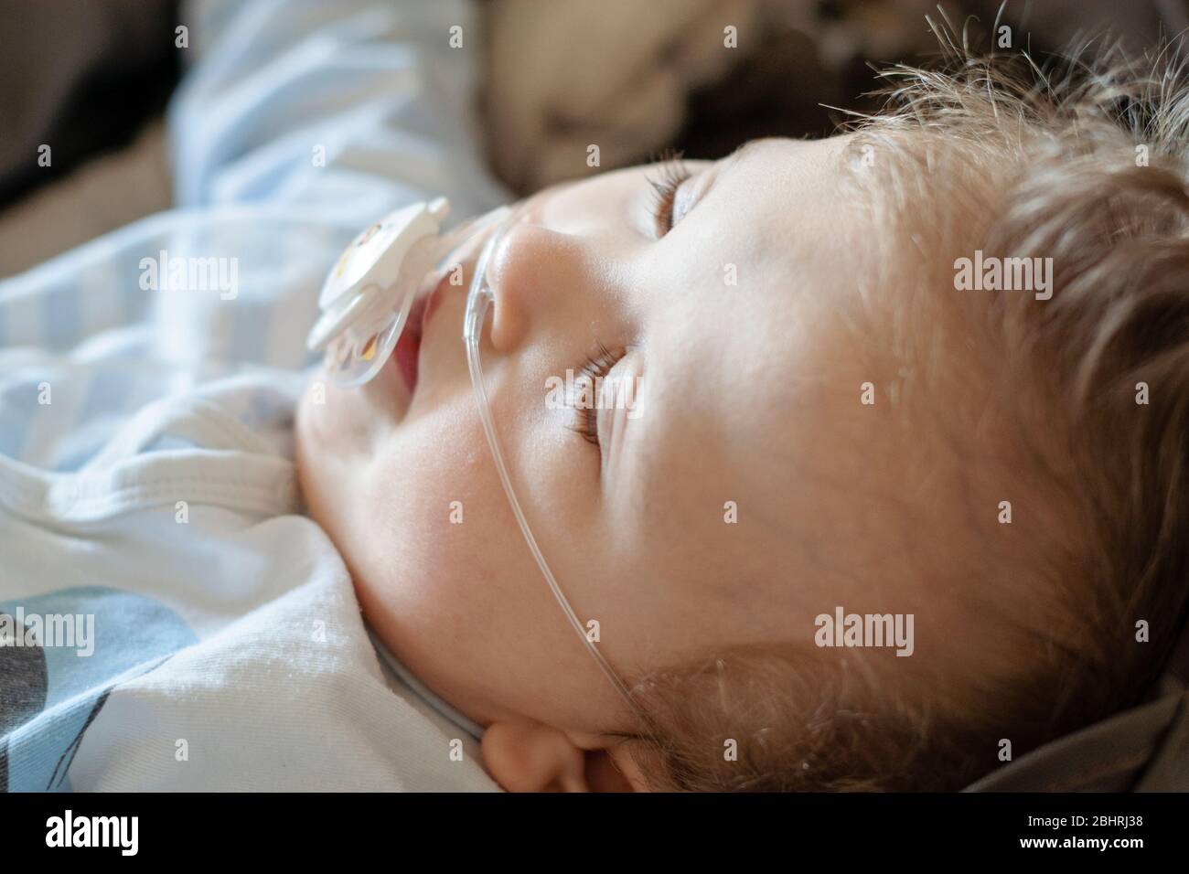 Baby boy with cerebral palsy is getting oxygen via nasal prongs to assure oxygen saturation. Nasal catheter in a child patient in hospital. Respirator Stock Photo