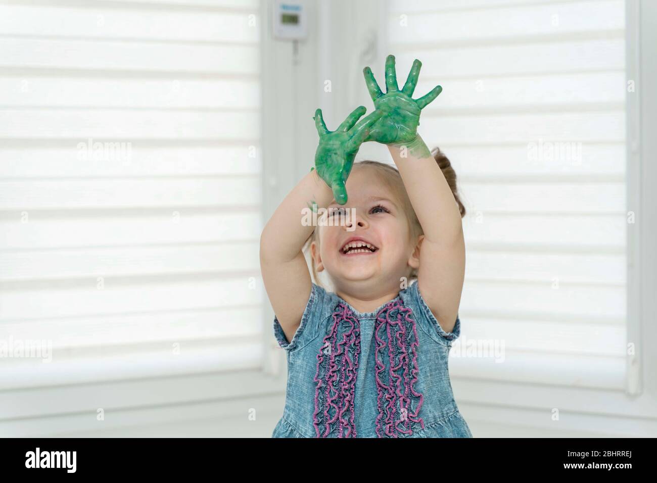 Little girl paints with fingers.girl joyfully raised her hands in raska up, self-isolation, coronavirus covid-19, stay home Stock Photo