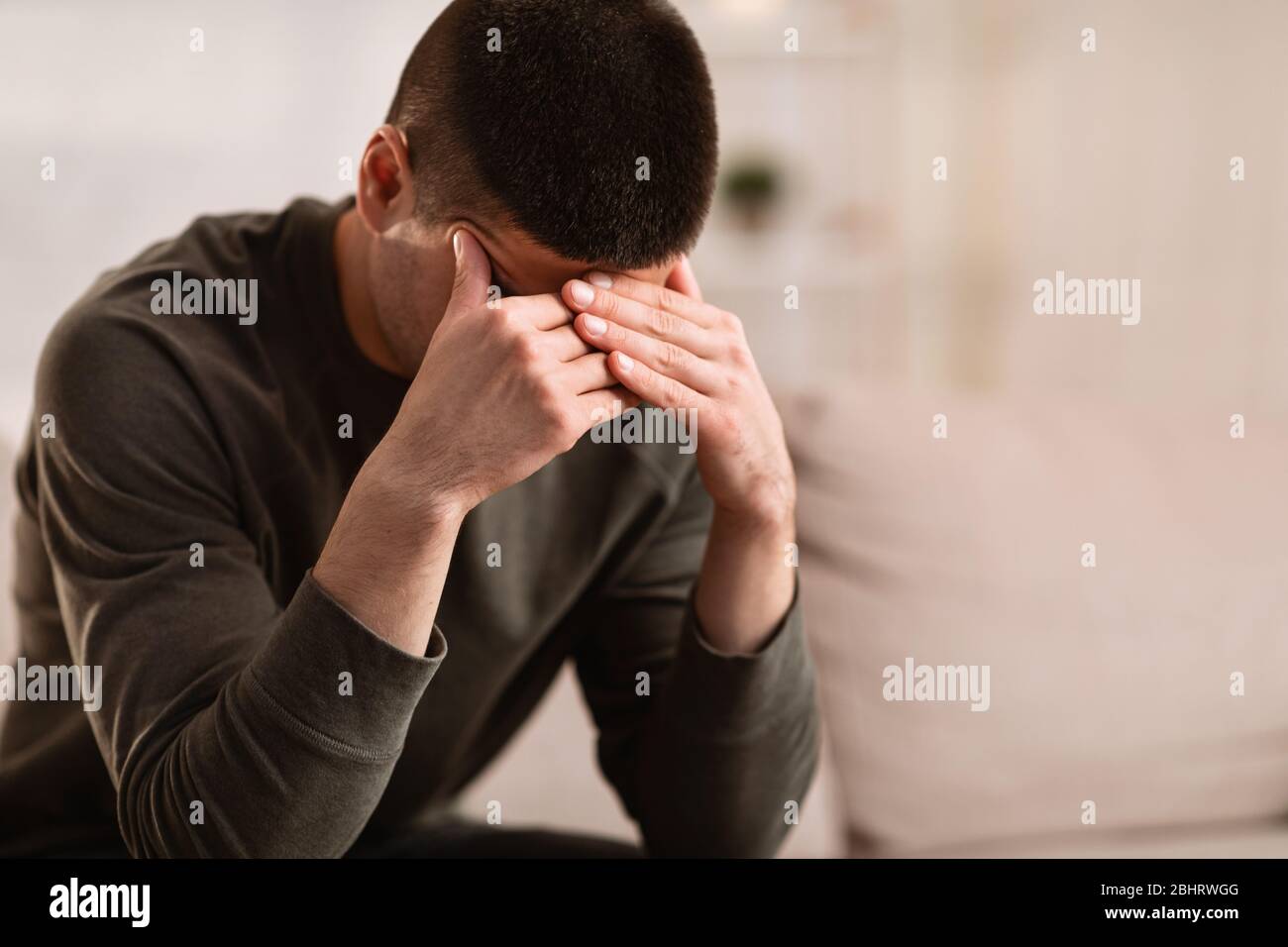 Ill man sitting on sofa with head on his hands Stock Photo