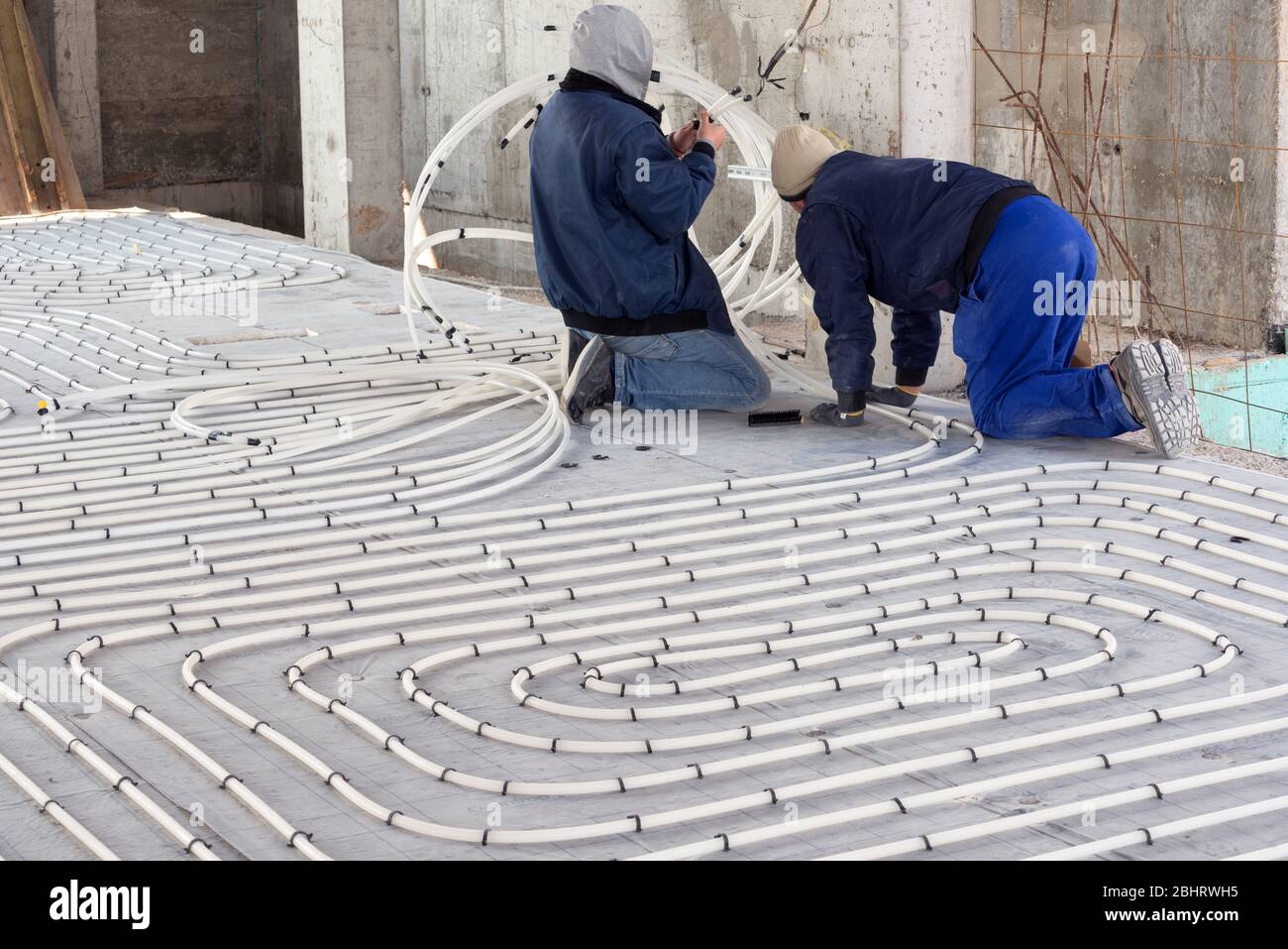 HVAC technicians working on underfloor heating system installation. Close up on water floor heating system interior of a new indoor swimming pool and Stock Photo