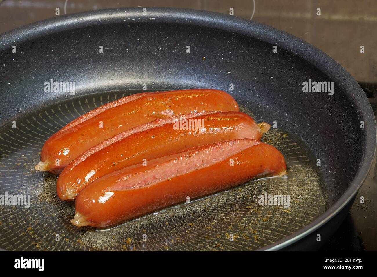 Frying sausage in hot olive oil at home kitchen close up. Top view of