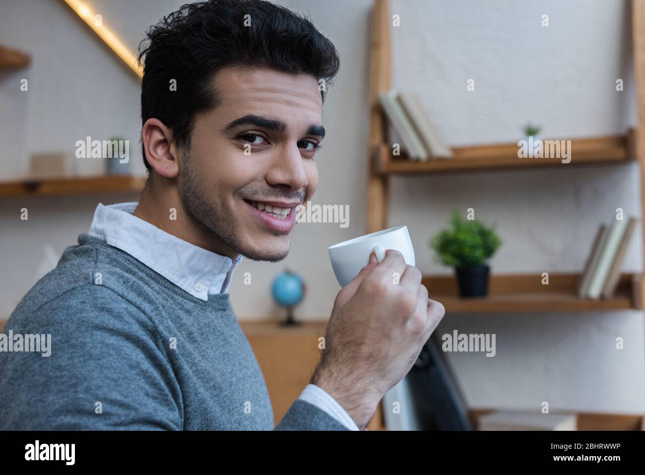 Businessman smiling, looking at camera and holding cup of coffee in ...