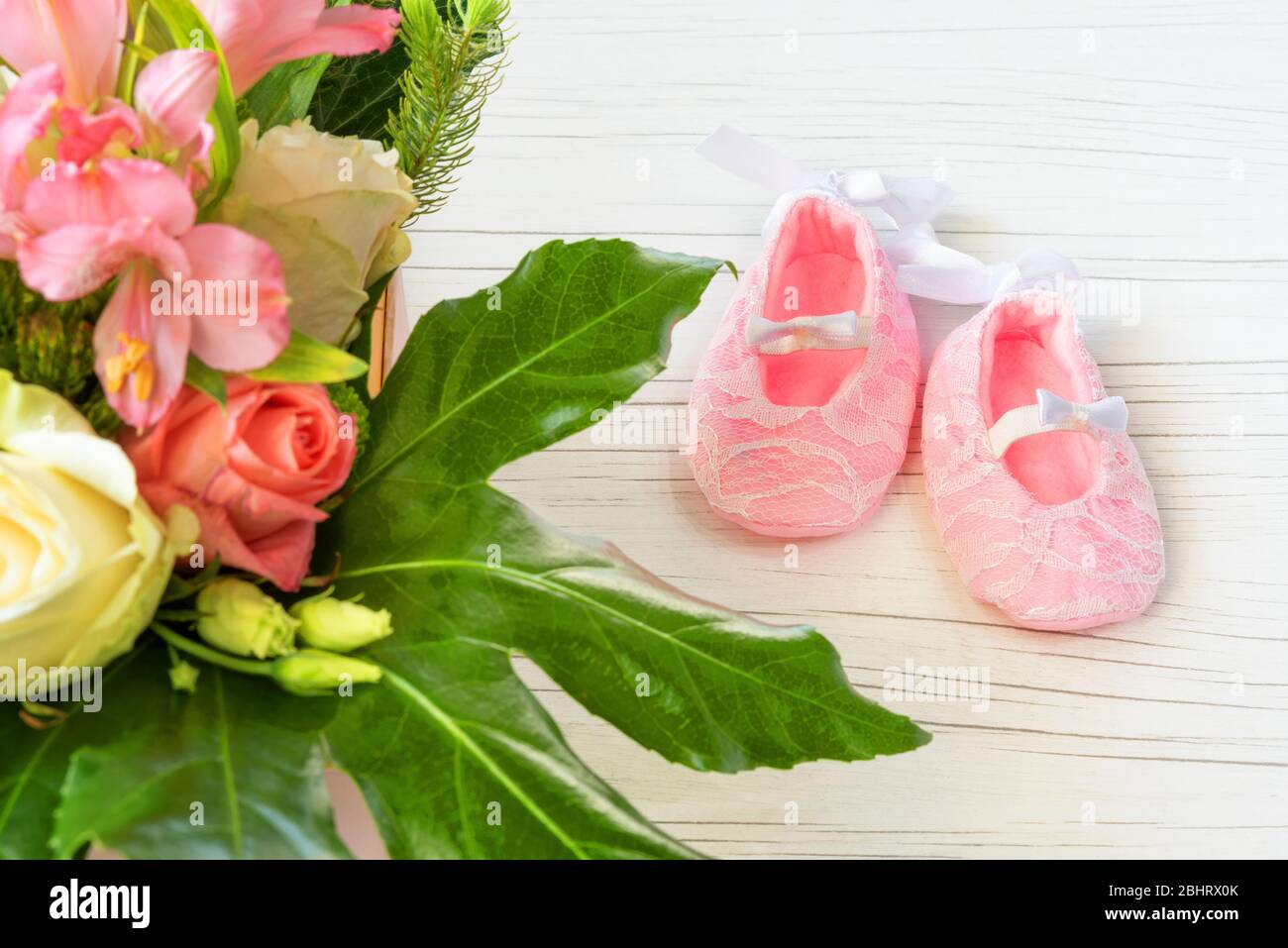 First pink shoes for little princess. Baby shoes with a basket with bright flowers. Wicker basket of flowers on a light background, beautiful fragrant Stock Photo