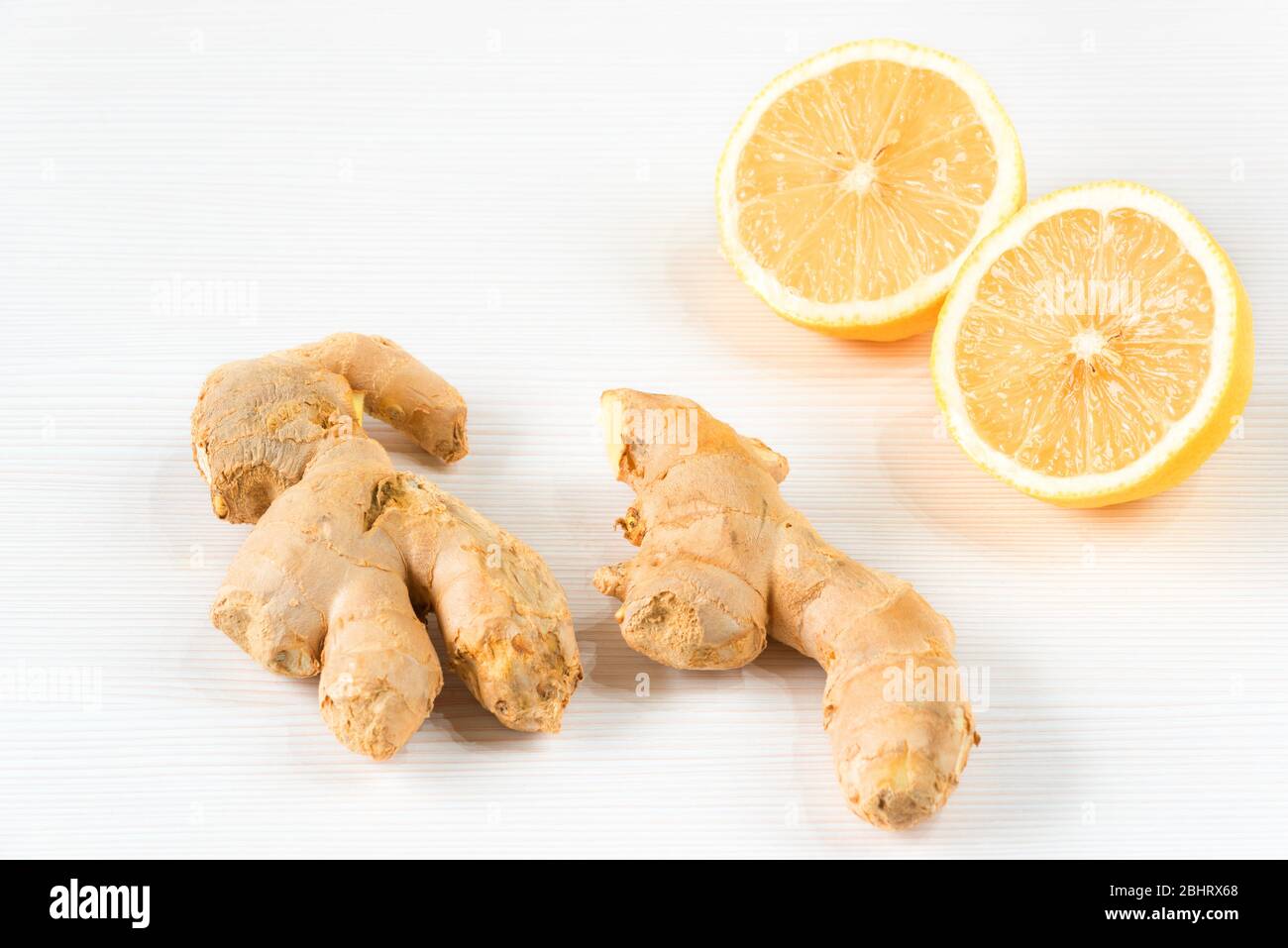 Closeup image of ingredients for natural cold or flu remedy includes ginger and lemon on a white wooden background. Selective focus on front slice of Stock Photo