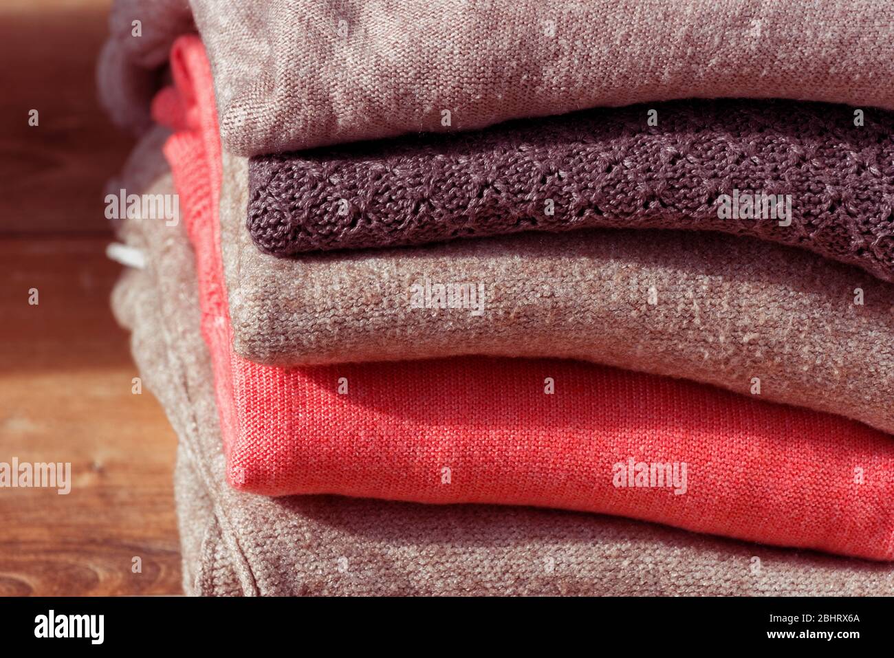 Stack of folded beige and pink clothes on brown wooden background. Female blouses pile. Stock Photo