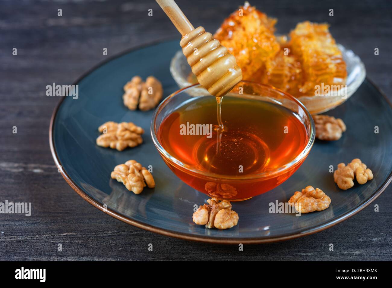 Image of honey dripping from honey dipper in glass bowl. Thick honey dipping from the wooden