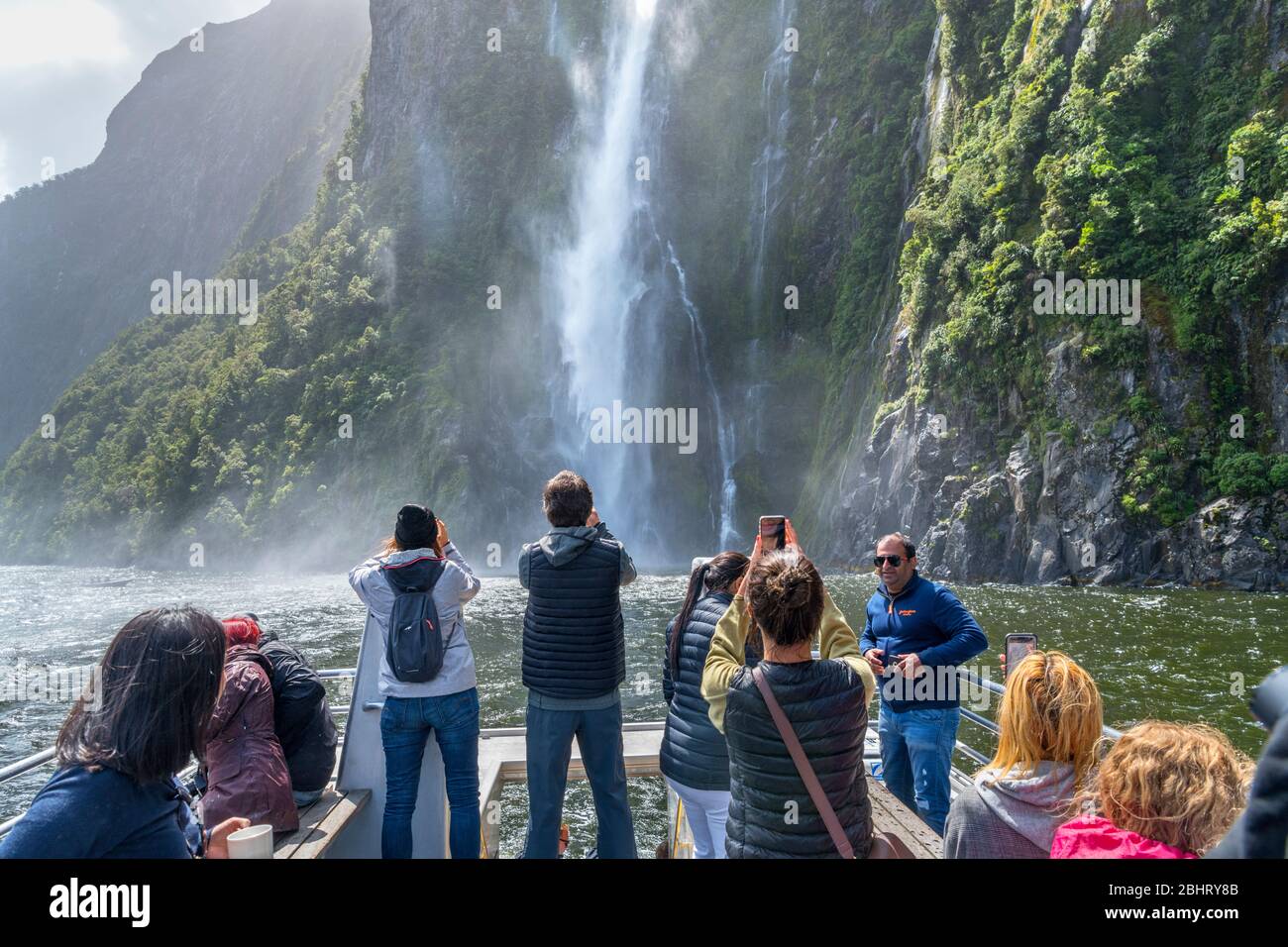 Milford Sound, New Zealand. Tourists photographing Stirling Falls from the deck of a cruise boat, Milford Sound, Fiordland National Park, New Zealand Stock Photo