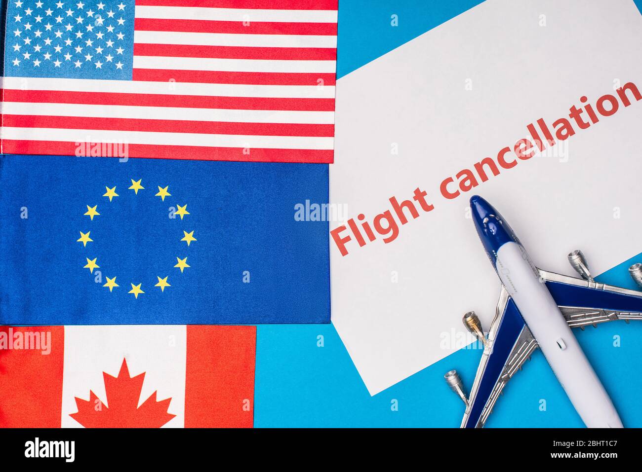 Top view of flags of canada, european union and america near toy plane with flight cancellation lettering on card on blue surface Stock Photo