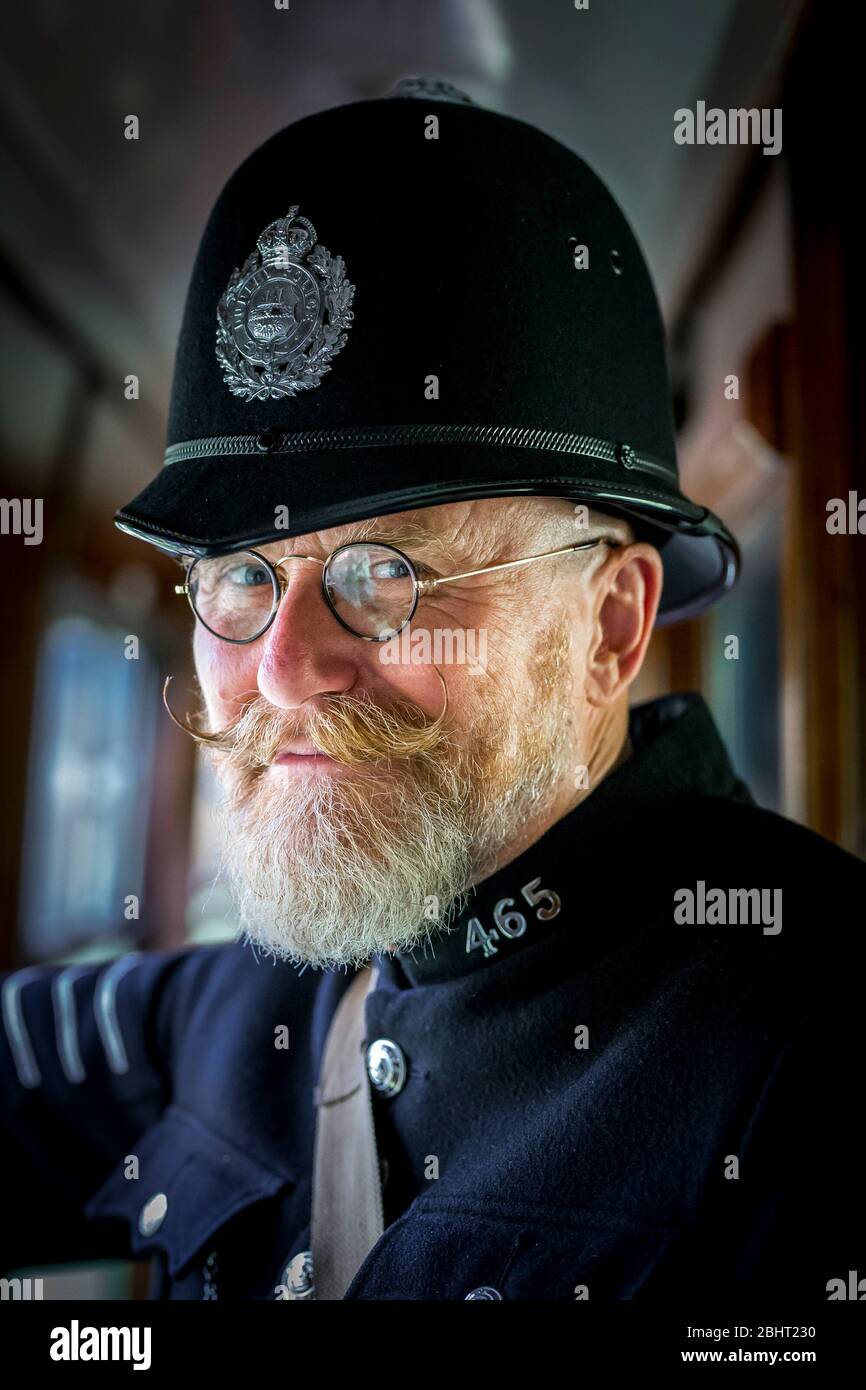 Close up of 1940 man as vintage UK policeman, in helmet, inside vintage railway carriage on board steam train, heritage railway WW2 1940s event UK. Stock Photo