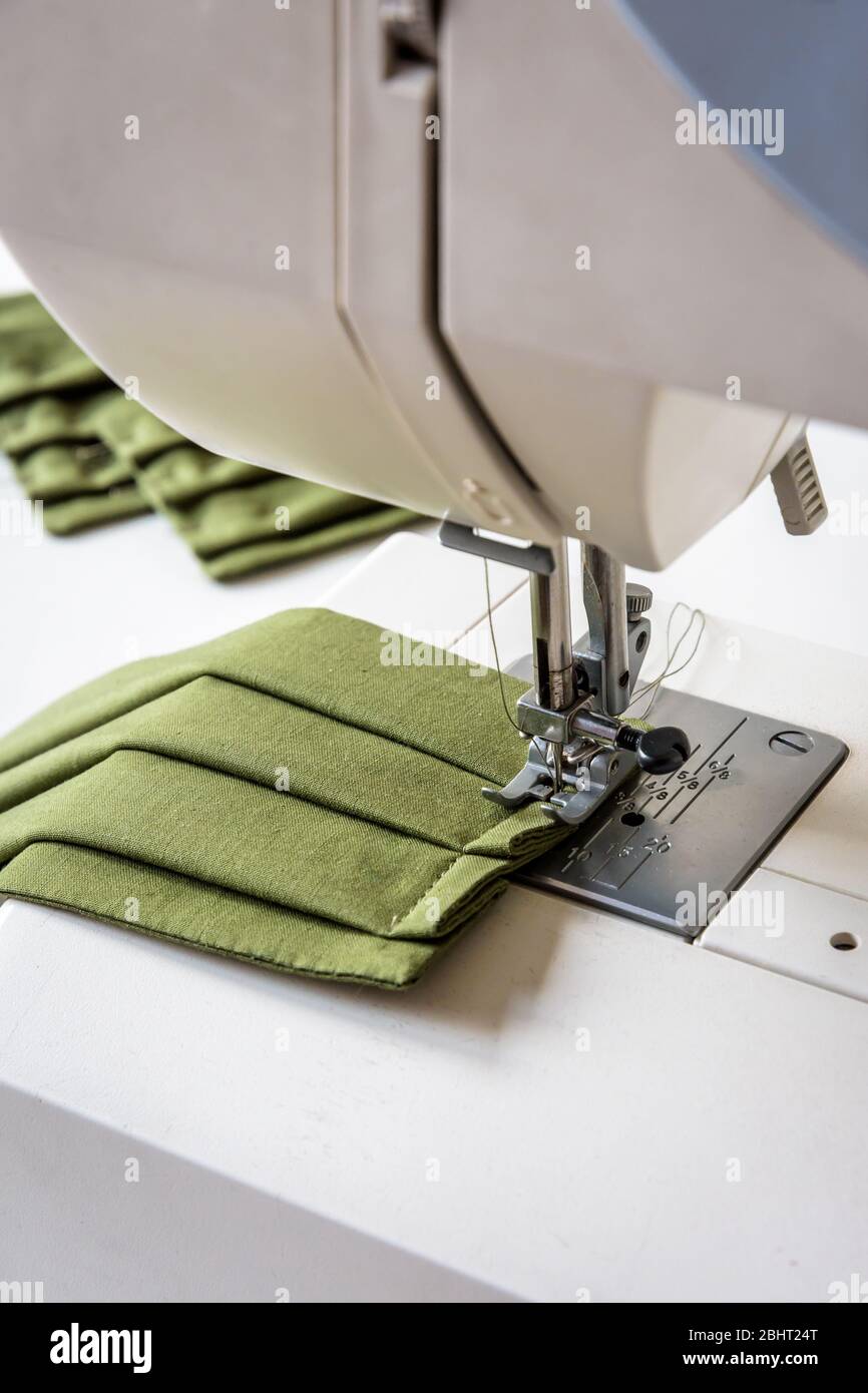 Close-up view on a homemade reusable cloth face mask in green cotton fabric being sewn on a sewing machine. Stock Photo