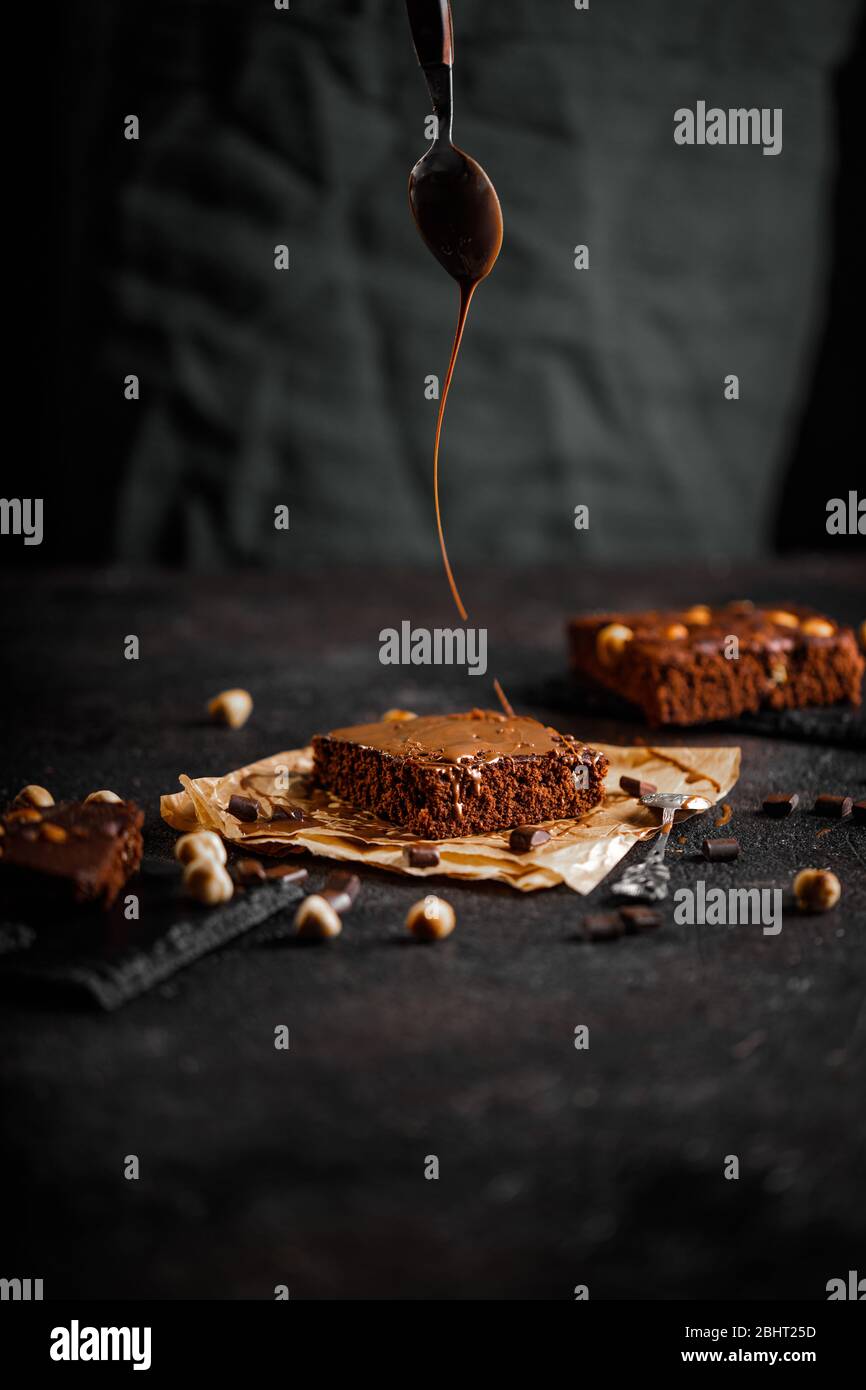Dark chocolate and cocoa brownie cake on light gray concrete table, pieces of chocolate and hazelnut Stock Photo