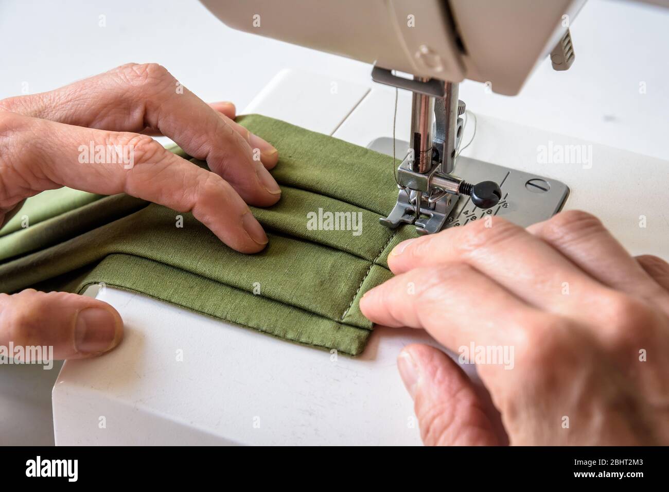 Close-up view on the hands of a woman sewing homemade reusable cloth face coverings in green cotton fabric on a sewing machine. Stock Photo