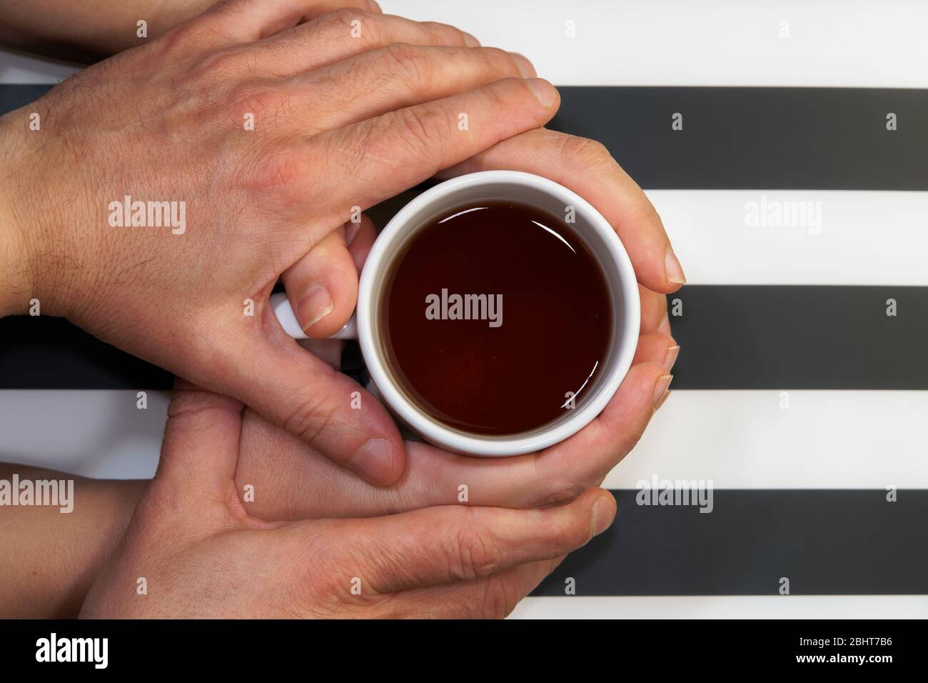 Loving couple on relationship, affectionately holding hands over beverage cup top view.Male tenderly touching female hands that hold a tea mug at home Stock Photo