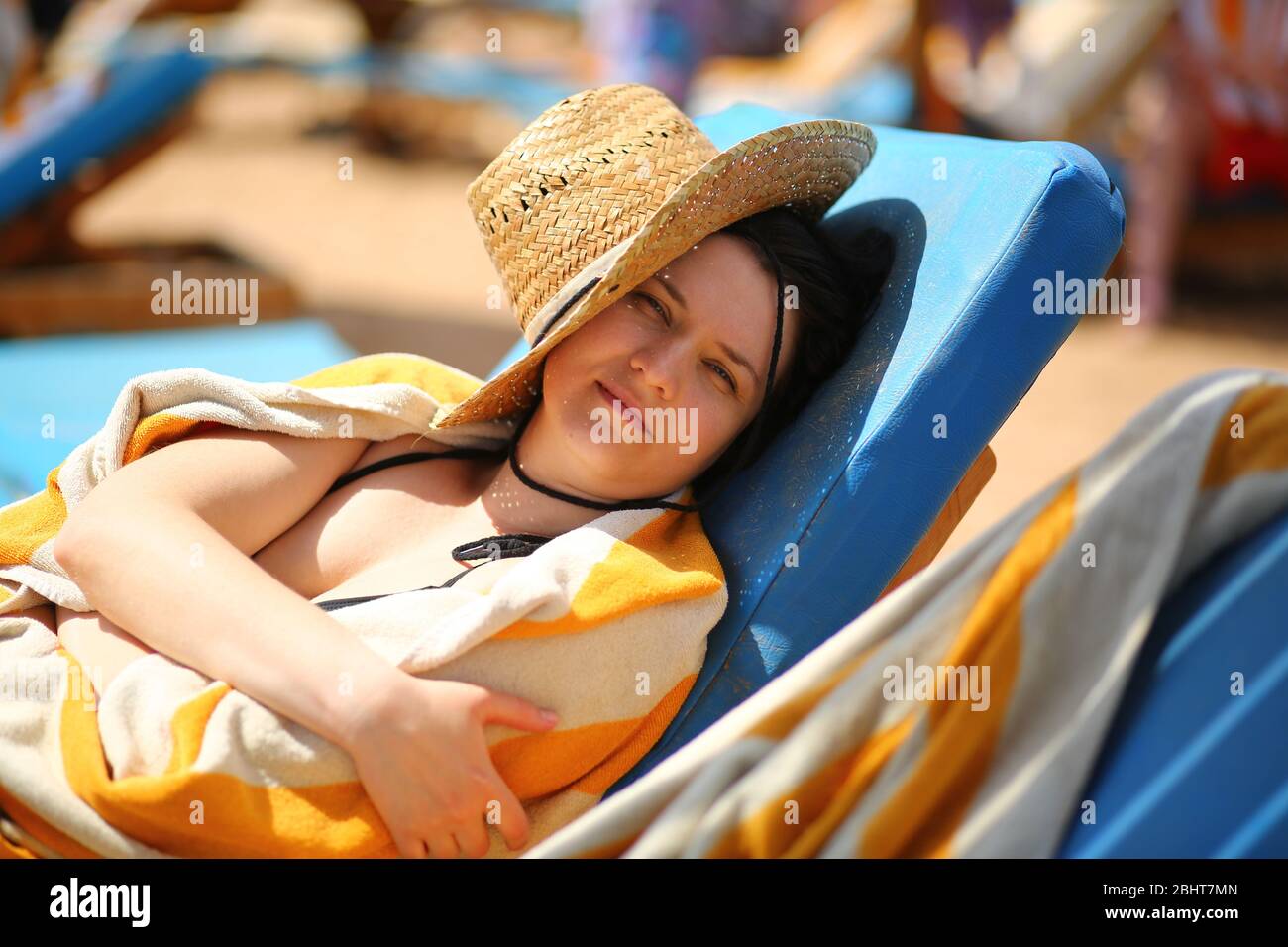 Portrait of a beautiful caucasian woman in 30s lying on the beach sun lounger and hiding from the sun behind the straw hat Stock Photo
