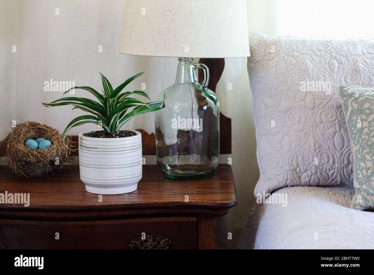 Farmhouse style bedroom with potted White Jewel, houseplant on an antique washing stand by a comfortable bed. Homemade lamp on dresser. Stock Photo
