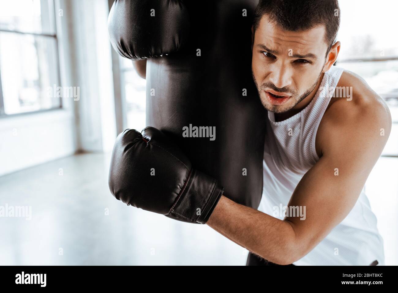 tired sportsman in boxing gloves touching punching bag and looking at