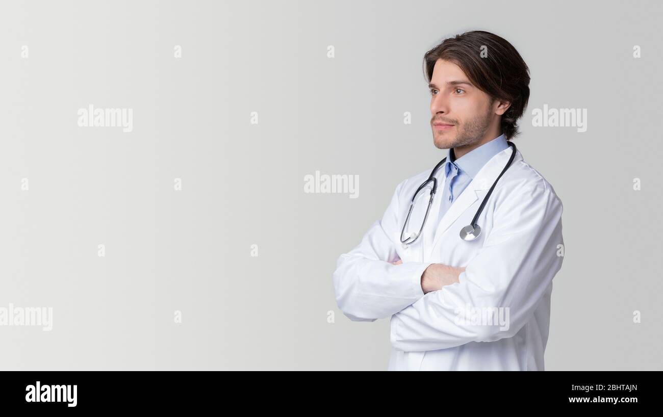 Portrait Of Thoughtful Male Doctor Standing With Folded Arms And Looking Away Stock Photo
