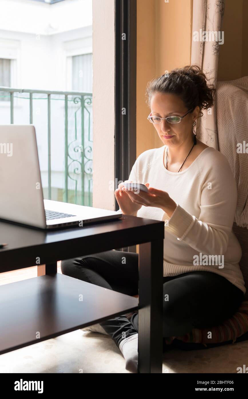 A woman sitting by a window in front of a laptop, telecommuting. Stock Photo