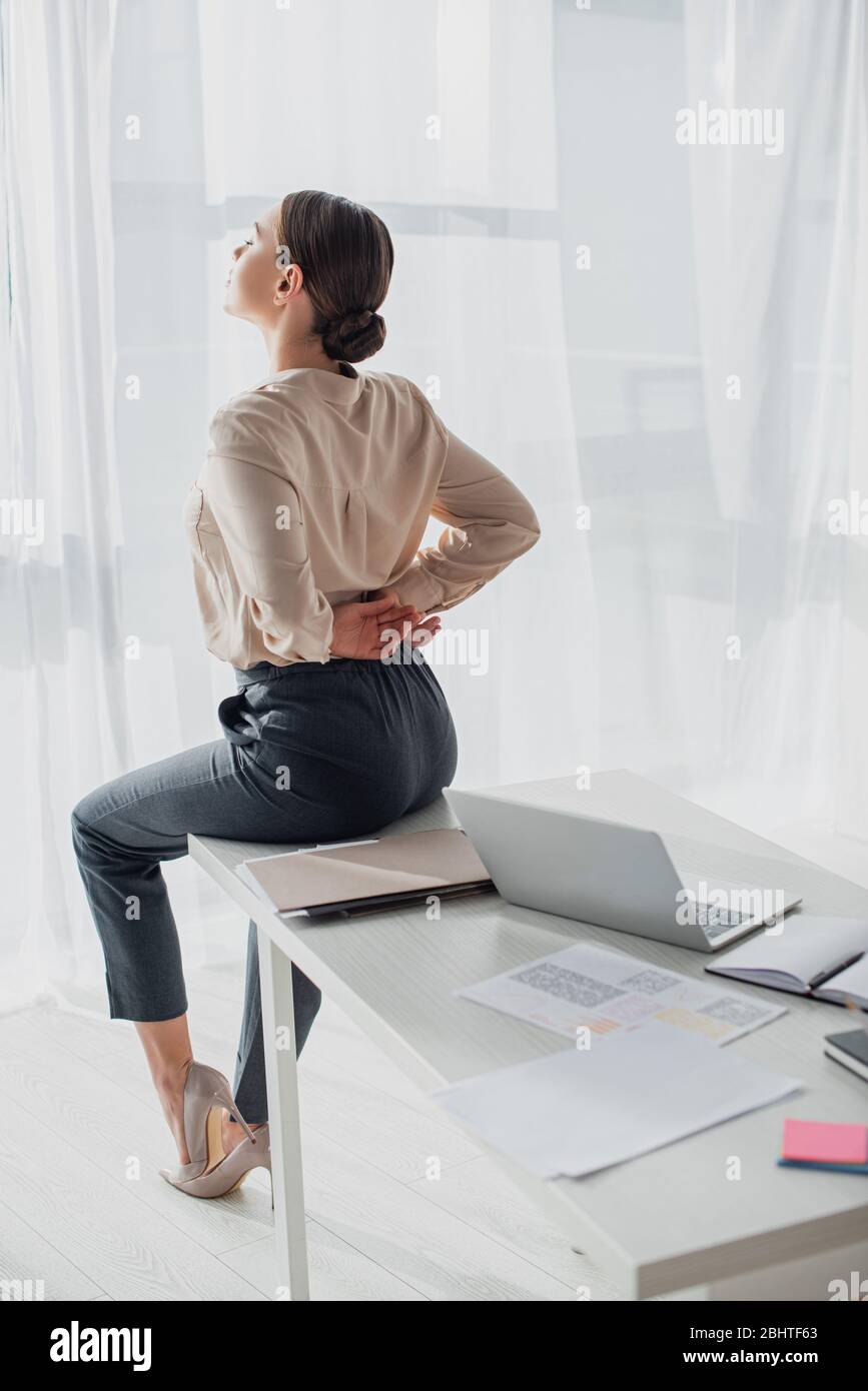 tired businesswoman stretching back on workplace with laptop Stock Photo