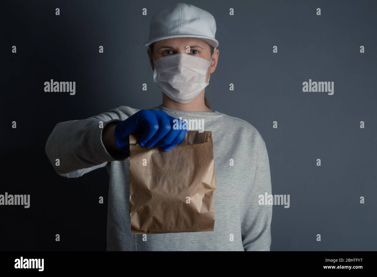 Safe food or goods delivery. Young courier delivering small brown eco paper bag order to the home of customer with mask and gloves during the coronavi Stock Photo