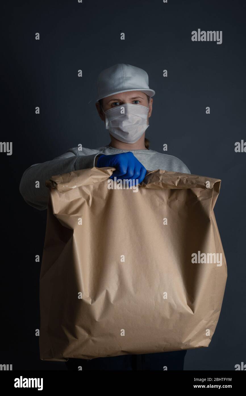 Safe food or goods delivery. Young courier delivering grocery big brown eco paper bag order to the home of customer with mask and gloves during the co Stock Photo