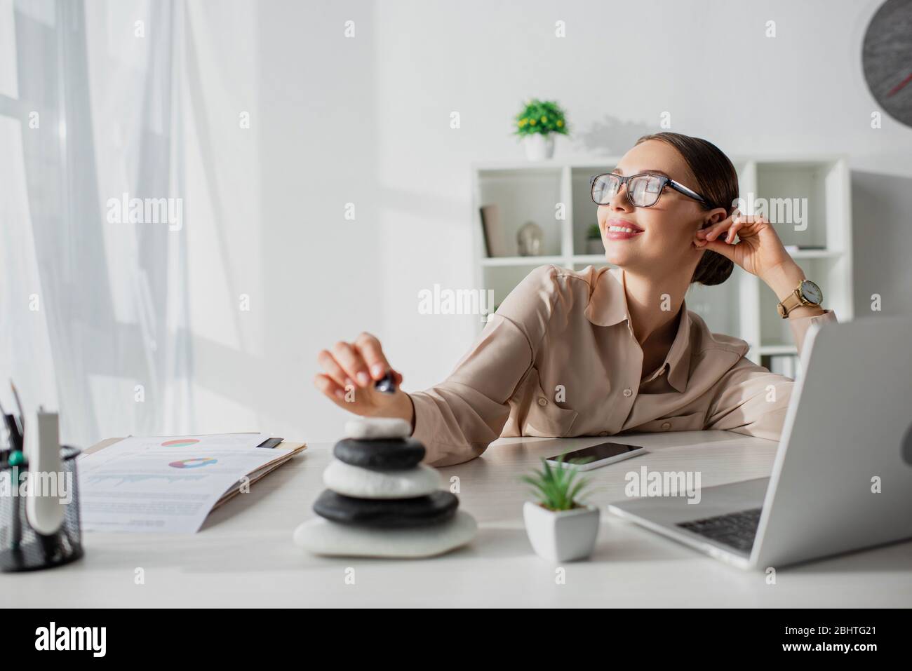 dreamy businesswoman sitting at workplace with zen stones and laptop