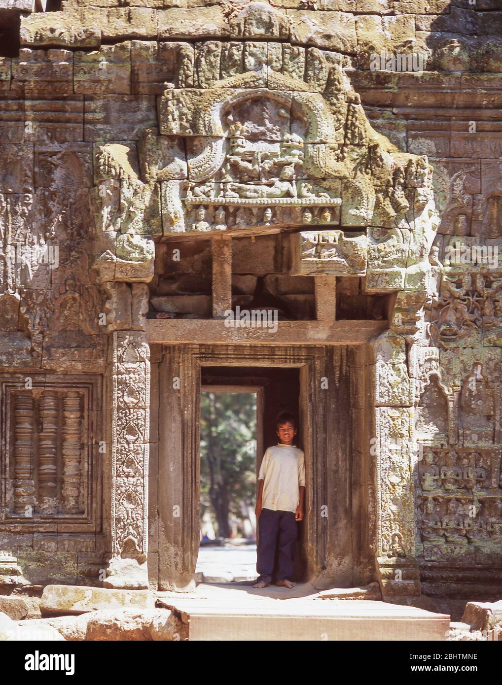 Young boy standing in ancient doorway, Ta Prohm Temple, Siem Reap, Kingdom of Cambodia Stock Photo