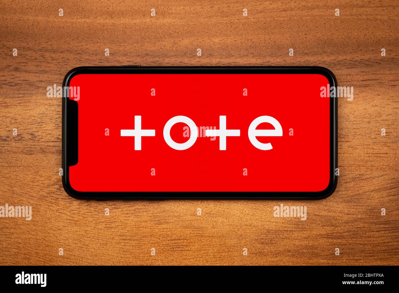 A smartphone showing the Tote logo rests on a plain wooden table (Editorial use only). Stock Photo