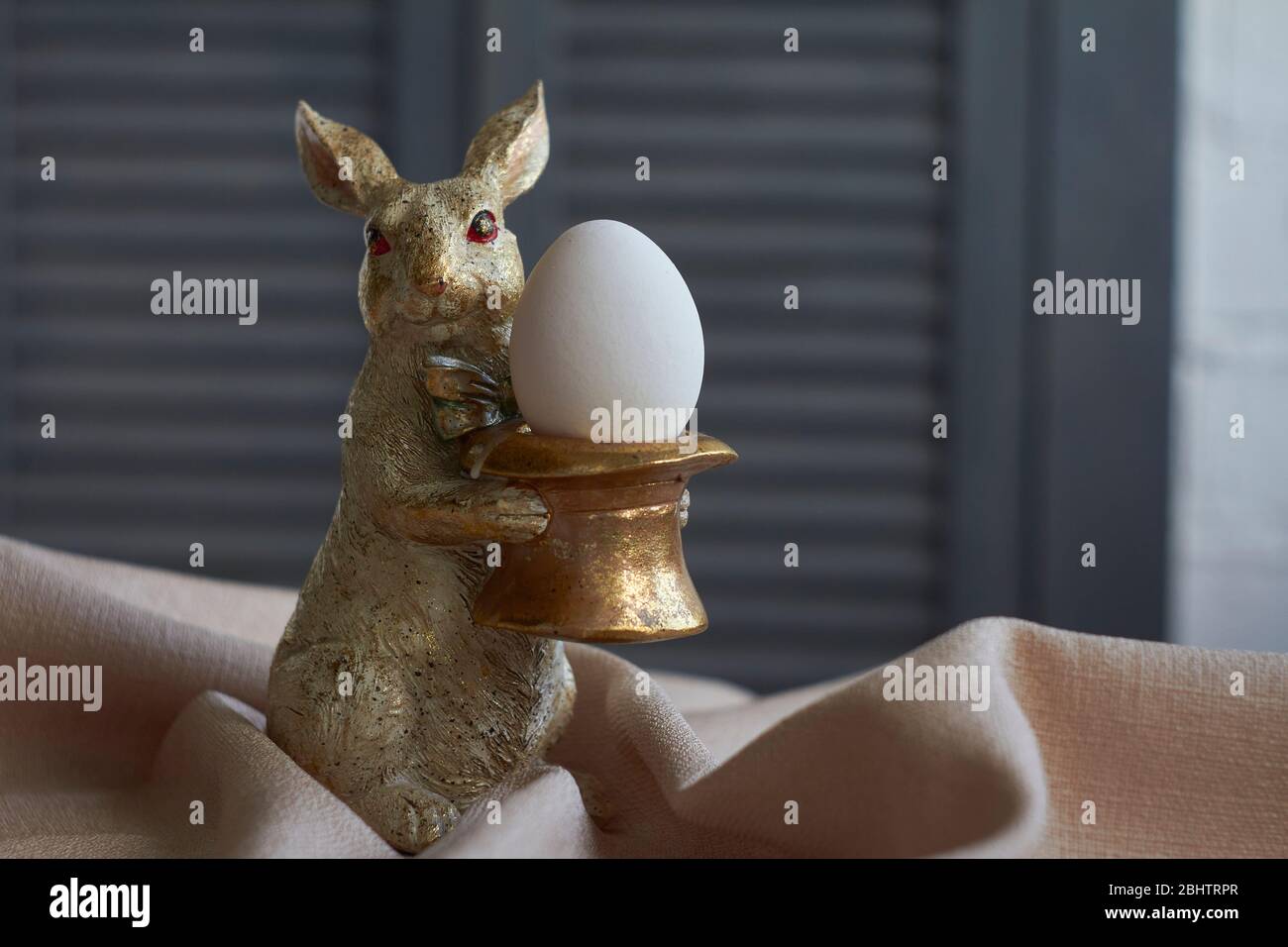 Spring composition, golden rabbit figurine with egg on beige tablecloth, Easter concept, selective focus Stock Photo
