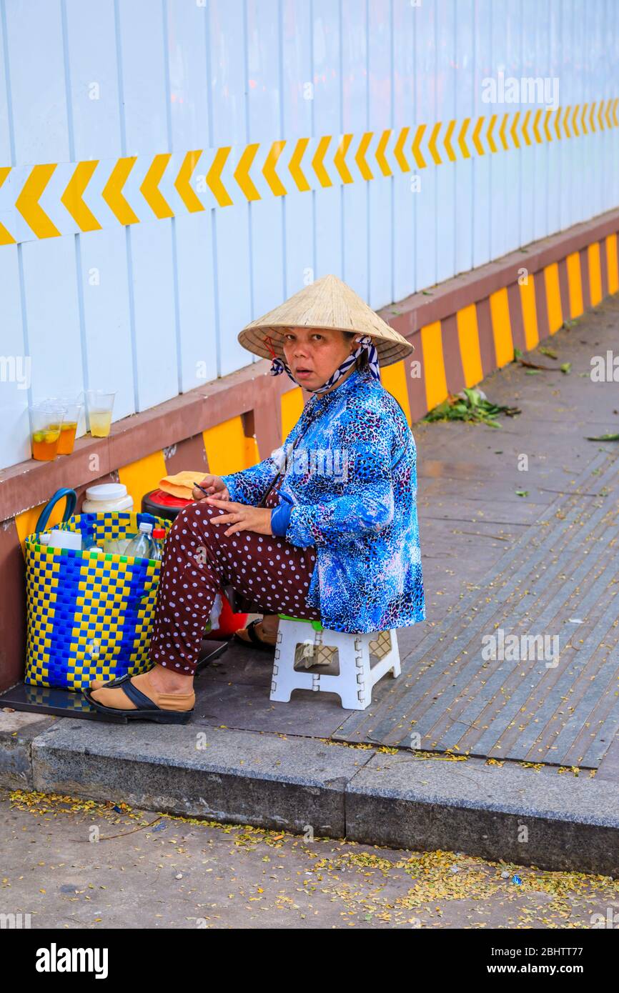 Local lifestyle: a woman wearing a straw conical hat sits with a basket of shopping: street view in Saigon (Ho Chi Minh City), south Vietnam Stock Photo