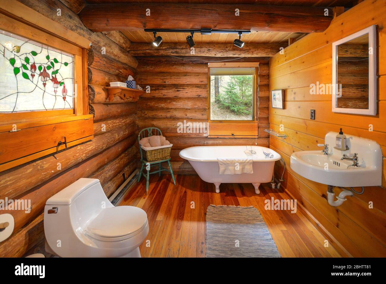 A bathroom in a rustic mountain log cabin home with sink, toilet and clawfoot tub. Stock Photo