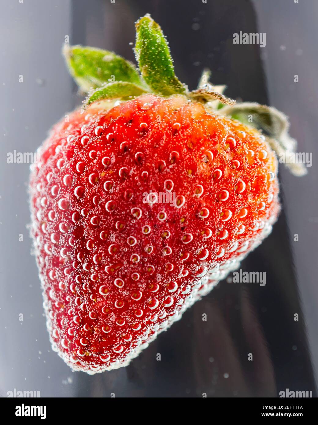 A ripe red strawberry submerged in a clear liquid with lots of bubbles.  Abstract reflections on the glass container. Stock Photo
