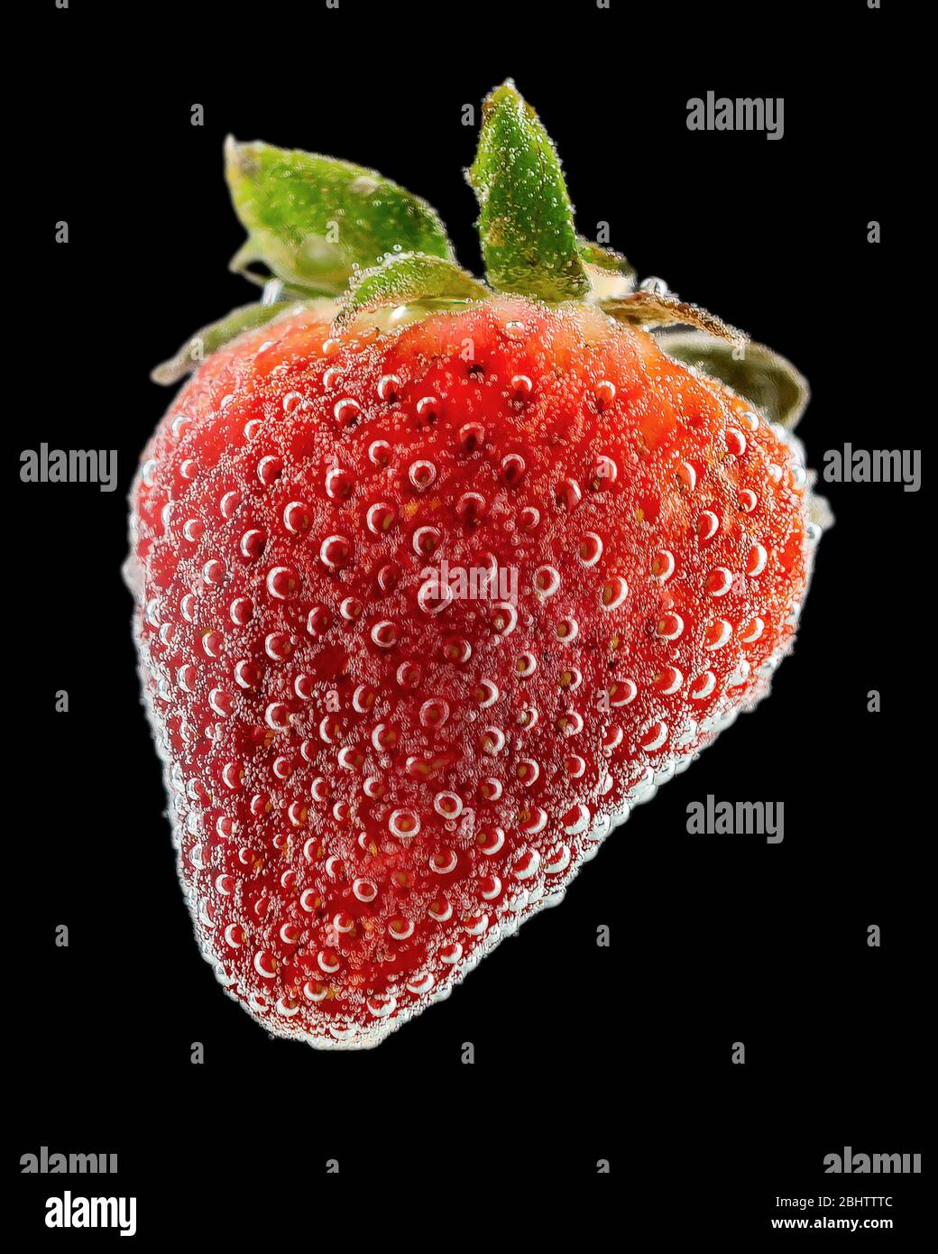 A ripe red strawberry submerged in a clear liquid with lots of bubbles.  Cut out on solid black background. Stock Photo