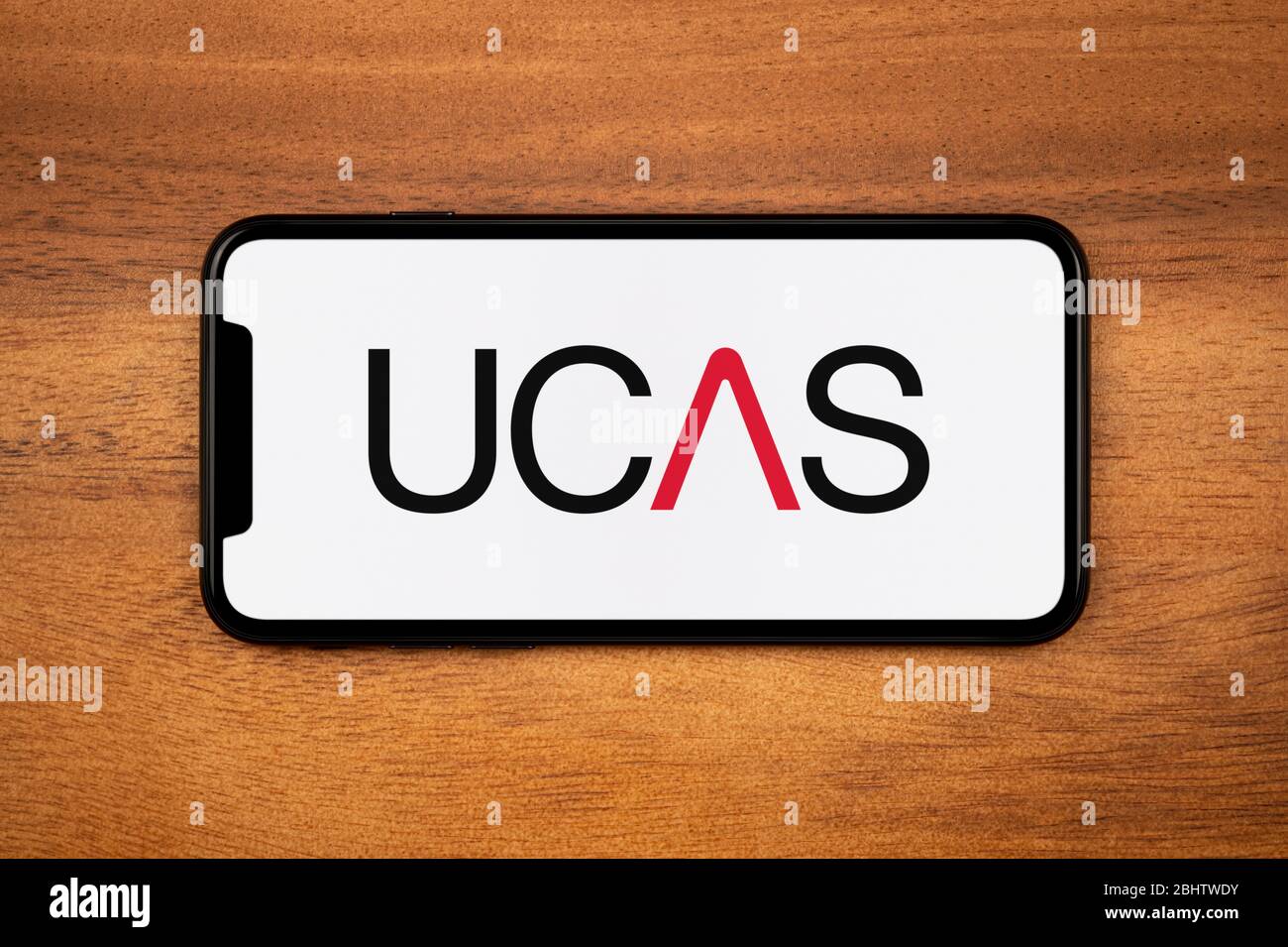 A smartphone showing the UCAS logo rests on a plain wooden table (Editorial use only). Stock Photo