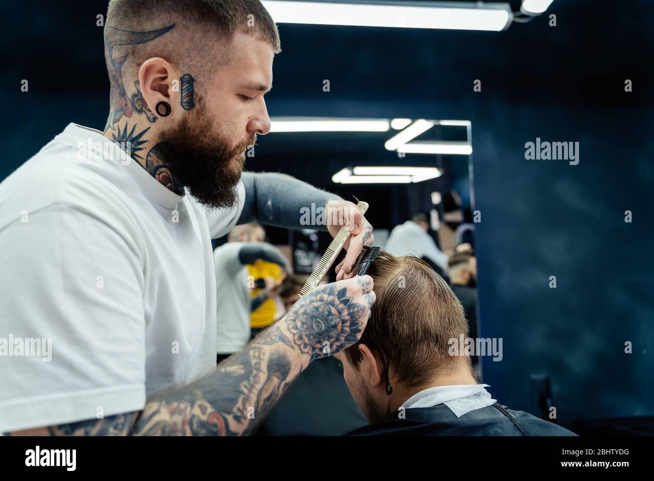 Professional tattooed barber using cutthroat razor cutting hair. Attractive  male is getting a modern haircut in barber shop. Close up Stock Photo -  Alamy