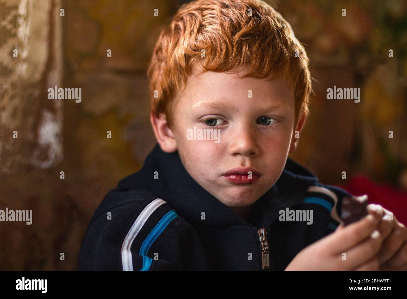 Portrait of unfortunate stray unclean kid. Hungry child with big clear eyes eating. Red-haired little boy. Close-Up. Concept of social problems. Life Stock Photo