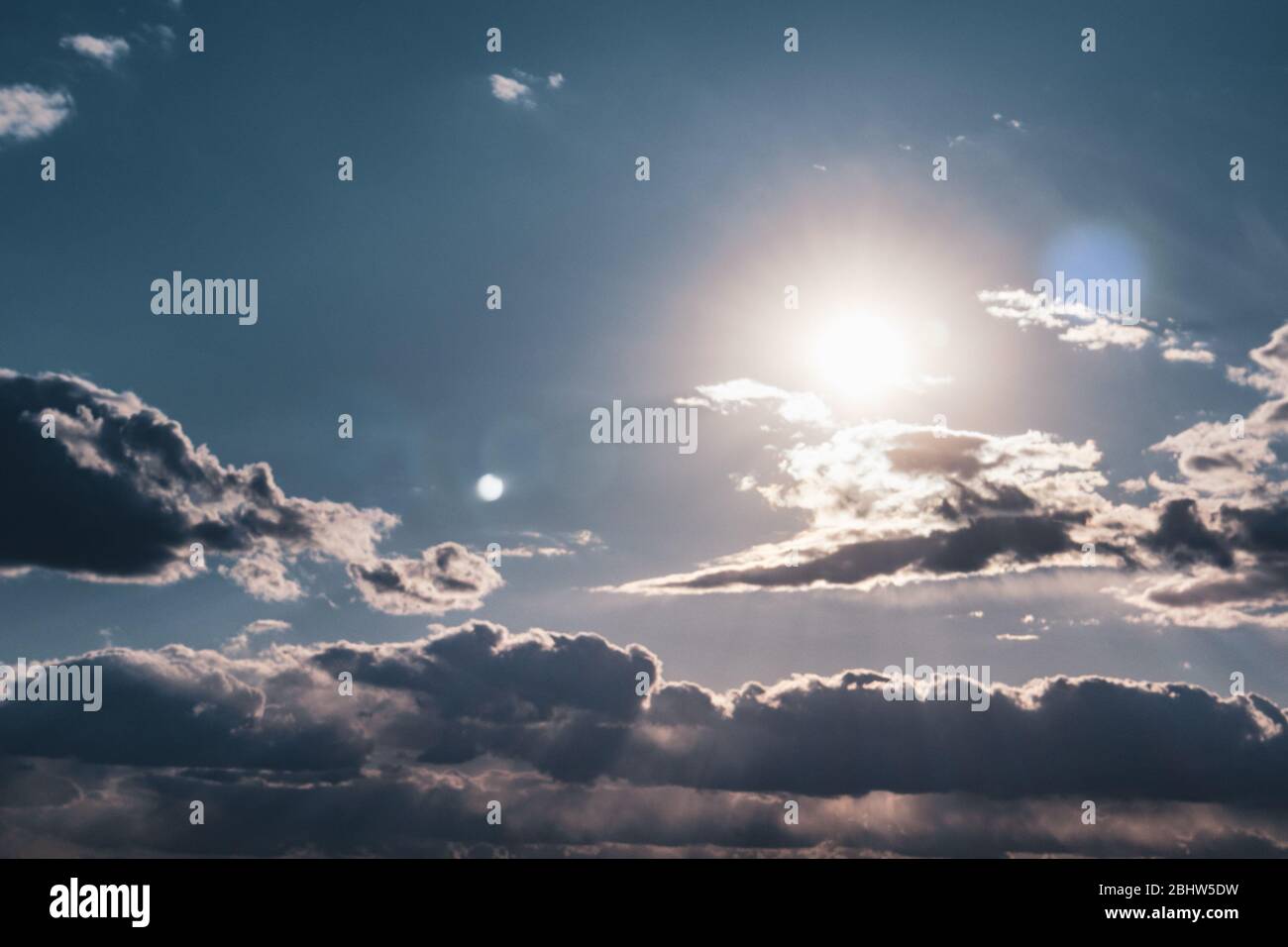 Scenic evening sun in clouds on blue sky. Sunlight in high large dramatic cloudscape moody background Stock Photo