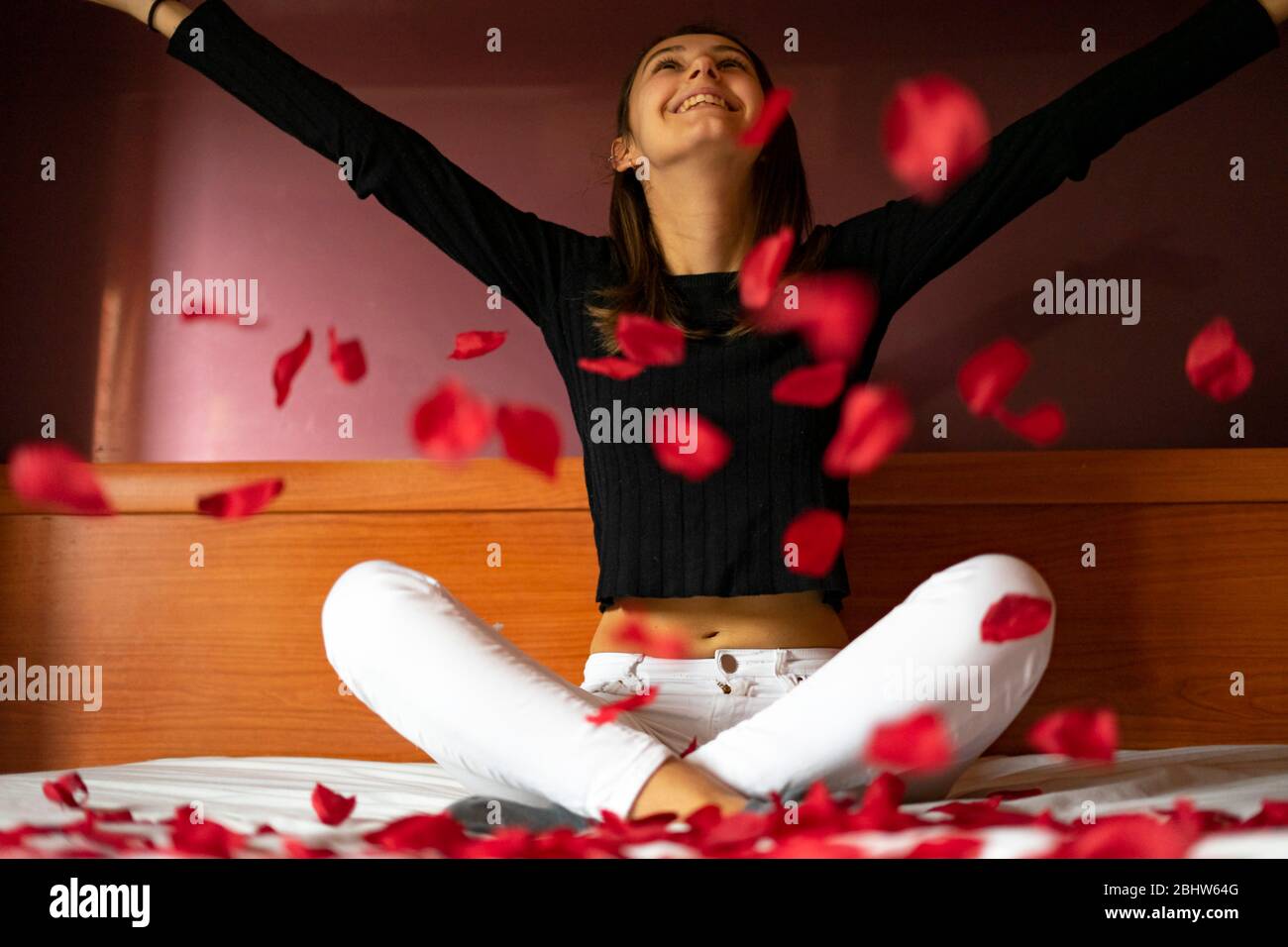 Woman throwing rose petals on the bed. Rose petals and happiness concept. Stock Photo