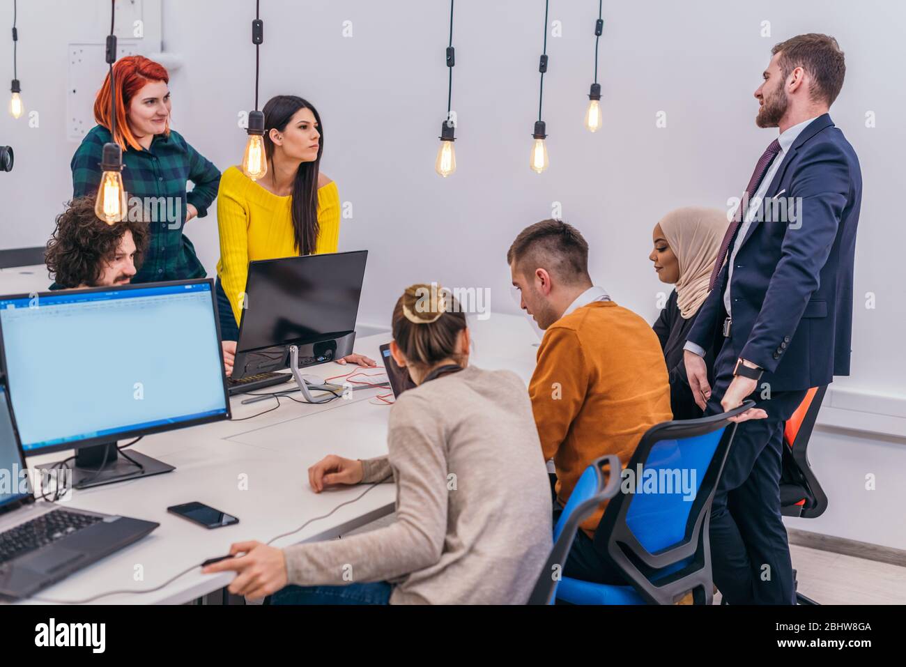 Handsome young executive explaining new employees an online task on theirs computers Stock Photo