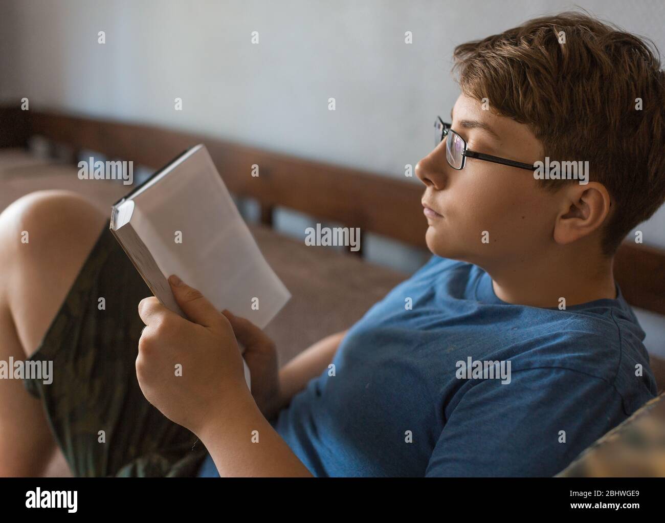 A teenager in glasses is reading a book at home. Knowledge and distance learning concept Stock Photo